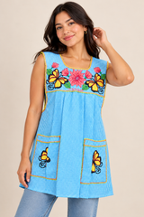 Woman modeling handmade baby blue gingham Mexican apron with butterfly and floral cross-stitch embroidery.