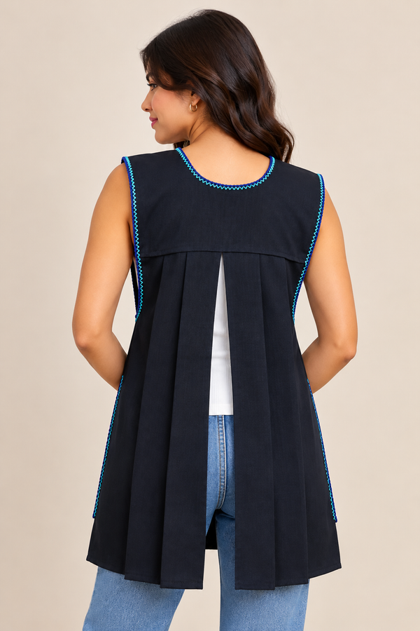 Back view of a black handmade Mexican apron with turquoise trim, pleated open-back design, modeled over a white top and jeans.