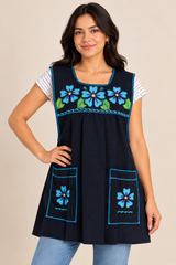 Young woman wearing a black Mexican apron with turquoise floral cross-stitch embroidery, decorative stitching, and two front pockets.