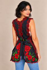 Back view of model wearing a black Mexican floral embroidered apron with red flowers, green leaves, and adjustable waist ties tied in a bow.