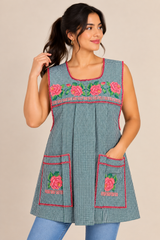 Mexican handmade green gingham apron with pink floral cross-stitch embroidery, modeled with front pockets and pink trim.