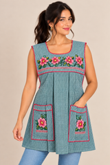 Woman wearing a handmade Mexican green gingham apron with pink embroidered flowers, two front pockets, and decorative stitching.