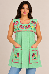 Front view of a handmade Mexican lime green gingham apron with pink floral embroidery, matching embroidered pockets, and decorative trim, modeled with blue jeans.