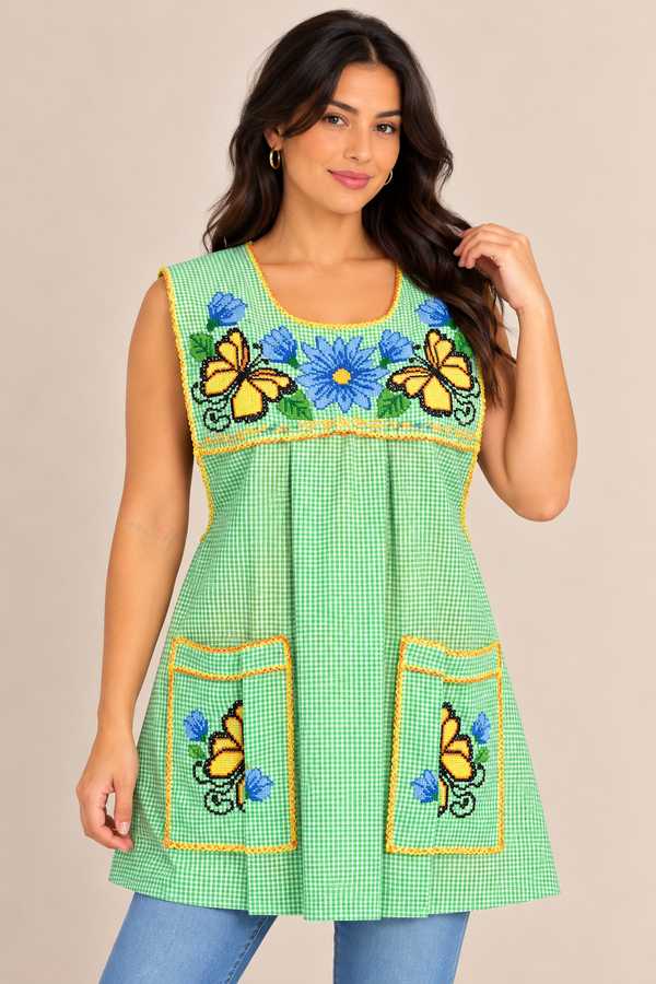 Model wearing a lime green gingham Mexican apron with colorful blue and yellow floral cross-stitch embroidery, two front pockets, and decorative trim.