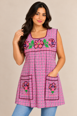 Front view of a handmade Mexican pink plaid apron featuring floral cross-stitch embroidery, two embroidered pockets, and a sleeveless design.