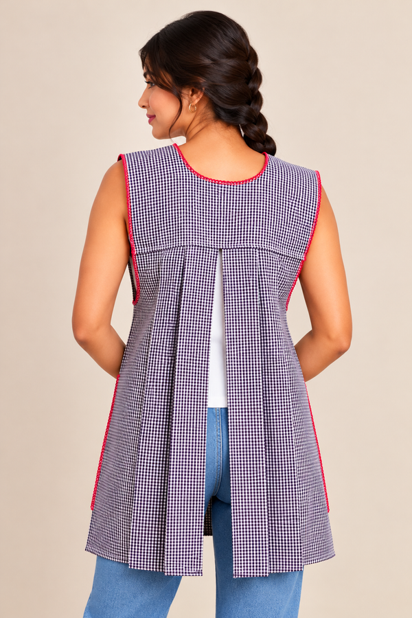 Back view of a purple gingham Mexican apron featuring an open-back design, pleated fabric, and decorative trim, modeled over blue jeans.