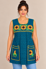 Model wearing a teal blue plaid Mexican apron with yellow sunflower cross-stitch embroidery, two front pockets, and yellow trim.